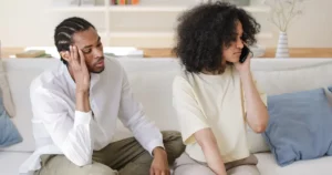 Homme inquiet observant sa compagne au téléphone sur un canapé : jalousie maladive dans le couple, thérapie de couple à Strasbourg
